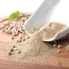 Finely ground White Pepper powder pouring from a white ceramic bowl onto a wooden cutting board.