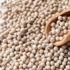 A macro shot of premium white peppercorns scattered around a wooden scoop.
